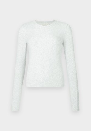 Šviesiai pilka ilgomis rankovėmis marškinėliai iš minkštos medvilnės audinio, suapvalintu kaklu ir prigludusiu siluetu. Lygus tekstūros paviršius su minimaliomis detalėmis.