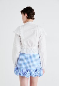 Hvit cropped bluse med spisskant og lange ermer, kombinert med en mini-skjørt i blå gingham med volangkant.