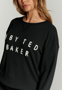 Čierna rebrovaná mikina so všitou výšivkou "BY TED BAKER" v bielej farbe. Priami strih s širokým výstrihom a dlhými rukávmi.