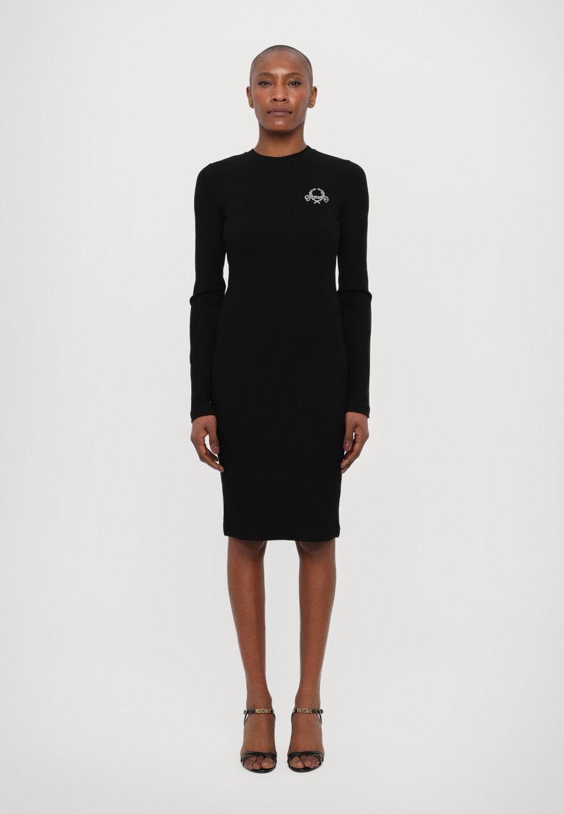 Rochie neagră cu mâneci lungi, cu un design ajustat, până la genunchi, având un mic logo brodat pe piept. Textură netedă, material elastic.