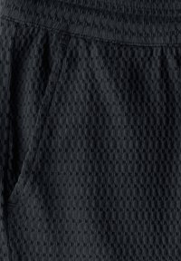 Svart texturerad tyg med rutmönster, med en synlig sidoficka och elastisk midja. Mjukt, vävt material med ribbad textur.