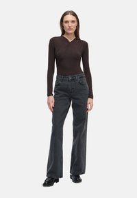 Brązowy bodysuit z długim rękawem w połączeniu z czarnymi spodniami dzwonami o wysokim stanie. Strój charakteryzuje się dopasowanym krojem i gładkimi fakturami. Czarne buty.