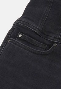 Gros plan sur la poche d'un jean noir en denim avec des coutures visibles et des rivets métalliques sur le tissu.