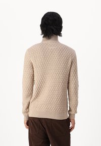 Pull en tricot beige avec motif texturé, col montant et poignets côtelés. Présente une coupe décontractée et une épaisseur moyenne pour la chaleur.