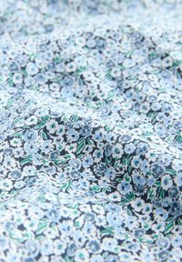 Viegls audums ar ziedu rakstu, kas satur zili un baltus ziedus uz tumša fona, ar zaļiem akcentiem un mīkstu tekstūru.