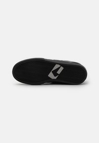 Semelle de basket noire avec une texture en chevrons, dotée d'un accent gris et d'un logo. Le matériau semble en caoutchouc pour une meilleure adhérence et durabilité.