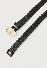 Cintura in pelle nera intrecciata con fibbia dorata a forma di D e estremità cucite, disposta in piano su uno sfondo chiaro.