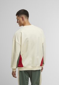 Fleece-Sweatshirt in Creme mit roten und grünen Akzenten. Verfügt über einen lässigen Schnitt, überschnittene Schultern und gerippte Bündchen. Glatte Textur.