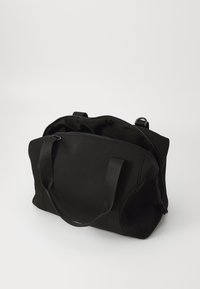 Bolsa de tela negra con una amplia abertura con cremallera, dos asas resistentes y un diseño minimalista; textura suave y sin marcas visibles.