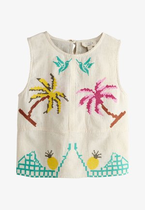 Jeune femme portant des lunettes de soleil et un haut sans manches assorti et un short à imprimé tropical, debout près d'un bar de plage rustique avec des ananas.