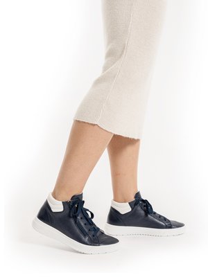 Legs wearing beige knit skirt and navy blue high-top sneakers with white soles and ankle collars, shown against white background.