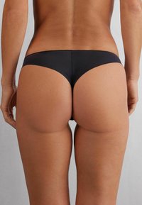 Parte inferiore di bikini nera con un taglio a vita bassa, texture liscia e copertura minima. Design semplice e elegante, senza hardware visibile o decorazioni.