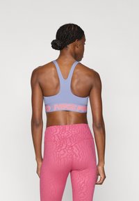 Μωβ αθλητικό σουτιέν με σχεδιασμό racerback και φαρδιά ροζ λωρίδα με το λογότυπο "NIKE PRO". Συνδυασμένο με ροζ ψηλόμεσα κολάν με υφή.