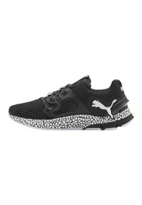 Chaussure de sport noire avec une tige en maille, semelle en caoutchouc texturée avec des accents blancs et un logo prominent sur le côté.