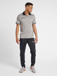 Polo grigio con colletto e polsini neri, abbinato a pantaloni da tuta neri con strisce laterali. Modello che indossa scarpe da ginnastica grigie.