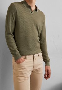 Olive green textured long-sleeve polo shirt with a collar, paired with beige slim-fit pants, featuring a front pocket.