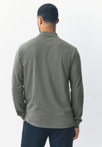 Tricou polo cu mânecă lungă, verde măsliniu, din țesătură moale. Are un guler tradițional și o croială lejeră cu tiv drept.