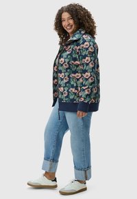 Felpa con motivo floreale su base verde scuro, fiori rosa e polsini a coste blu navy. Jeans a vestibilità ampia e sneakers bianche con accenti chiari.