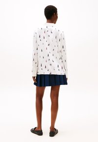 Chemise blanche à manches longues avec un petit imprimé de voilier, associée à une jupe plissée bleu marine et des chaussures noires. Design simple et épuré.