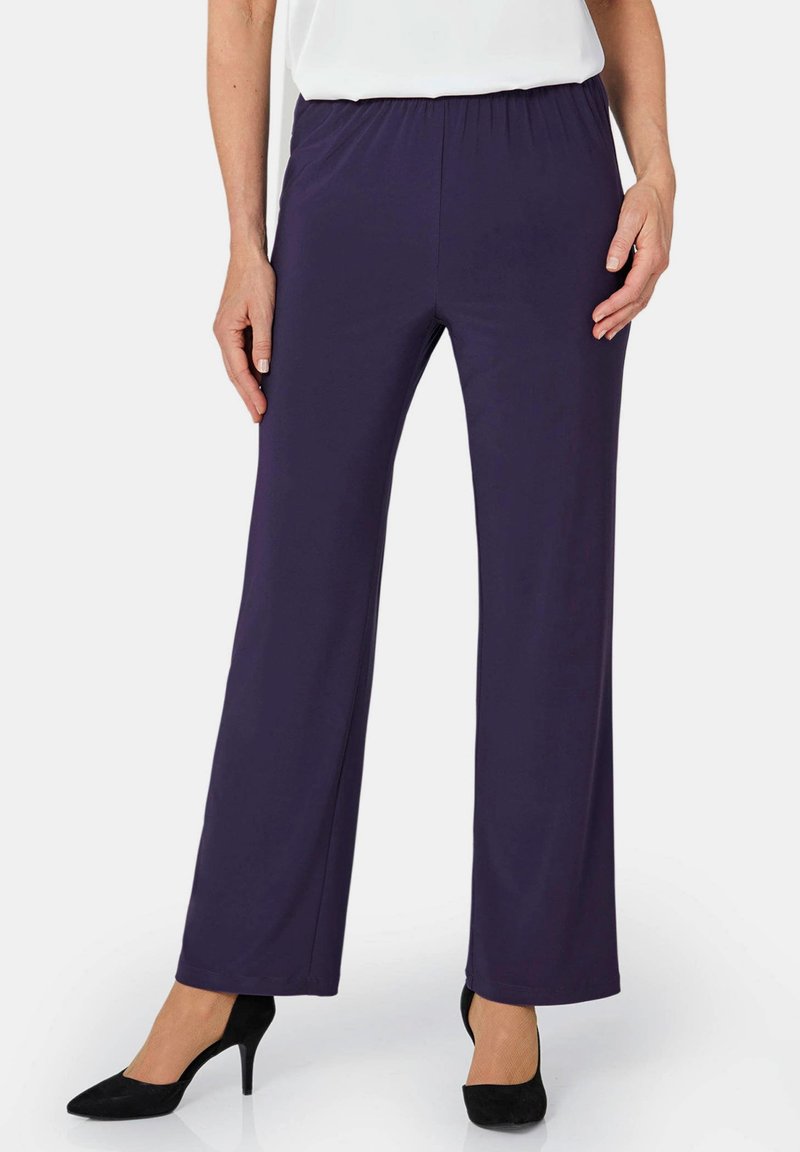 Marineblauwe high-waisted broek gemaakt van rekbaar materiaal, met een platte elastische tailleband en een rechte pijp, gecombineerd met zwarte hakken.