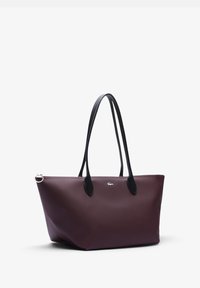 Sac fourre-tout en cuir bordeaux foncé avec des poignées noires, forme trapézoïdale, surface texturée et un accent de logo à l'avant.