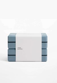 Des blocs de yoga bleus empilés avec une bande blanche étiquetée "BLOCS DE YOGA", présentant des surfaces texturées et des bandes noires en accent.