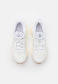 Scarpe da ginnastica bianche con una parte superiore in rete traspirante, lacci piatti e una suola in gomma chiara. Presentano un logo discreto e un design testurizzato sulla parte superiore.
