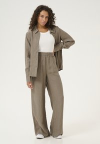 Beige ribbed button-up shirt paired with matching wide-leg pants, featuring an elastic waistband and a white tank top underneath.