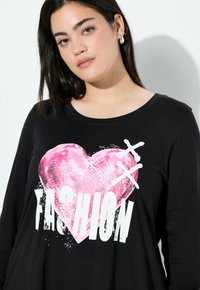 Czarna koszula z długim rękawem z dużą różową grafiką serca i białym napisem "FASHION". Miękka tkanina i luźny krój.