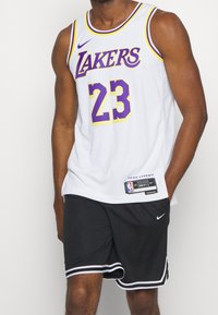 Weißes Basketballtrikot mit lila und gelben Akzenten, mit dem Text "LAKERS" und der Nummer "23". Schwarze Shorts mit weißem Rand und Nike-Logo.