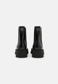 Bocanci negri din patent, cu panouri elastice pe laterale și o talpă texturată groasă. Include eticheta cu logo la spate și un design elegant și neted.