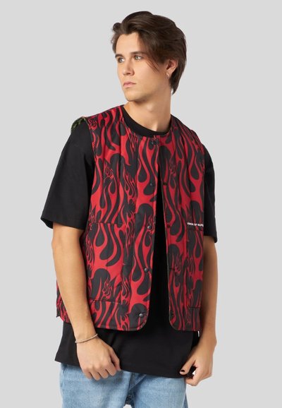 Gilet imbottito con motivo a fiamma rosso e nero, dotato di bottoni a pressione e una t-shirt nera a contrasto sotto.