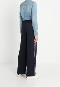 Námořnické kalhoty s širokými nohavicemi a elastickým pasem, s vícebarevnými pruhy po straně. Spárováno se světlou džínovou košilí a bílými teniskami.