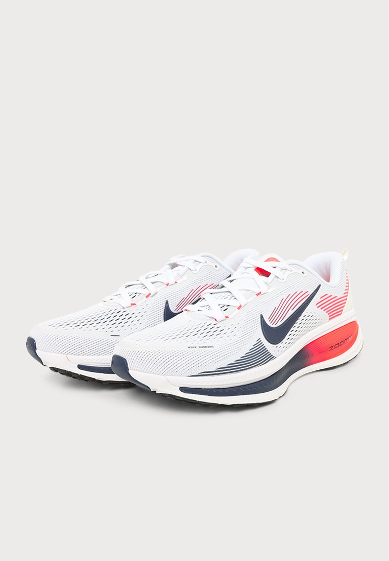 Un par de zapatillas de running Nike blancas con logotipos Swoosh azul marino, detalles rojos, parte superior de malla y suelas acolchadas sobre un fondo liso.