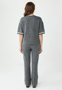 Grijs gebreid top en flared broekset, gemaakt van een textuurstof met witte afwerking op de mouwen, weergegeven vanuit de achterkant.