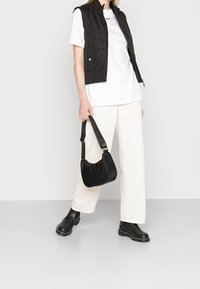 Svart pufferväst över en vit t-shirt, krämfärgade vida byxor, svart axelväska och svarta ankelboots. Släta texturer och funktionell design.