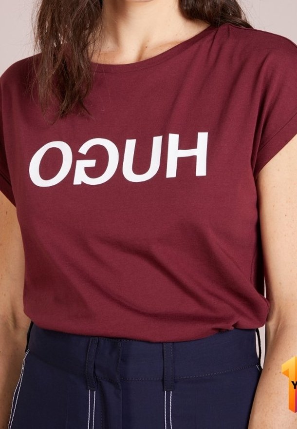 Camiseta burdeos de corte holgado, con el nombre de la marca "HUGO" en grandes letras blancas. Mangas cortas y textura de tela suave.