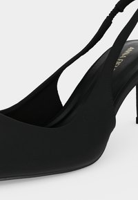 Μαύρο γοβάκι με μυτερή μύτη, λάστιχο και λεπτό τακούνι στιλέτο σε λευκό φόντο.