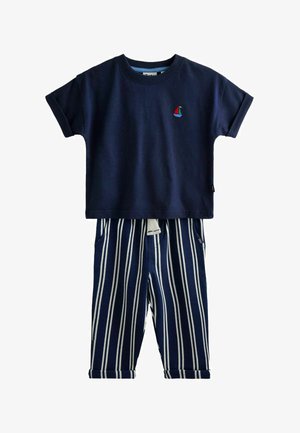 Tumesinine lühikeste varrukatega särk väikese punase ja sinise purjekagraafilise tikandiga, mida on kombineeritud tumesiniste ja valgete vertikaalsete triibuliste pükstega, millel on nööriga vöö.