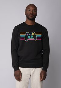 Zwarte sweatshirt met een kleurrijke gamecontroller-afbeelding en horizontale strepen in roze, geel en turquoise over de borst.