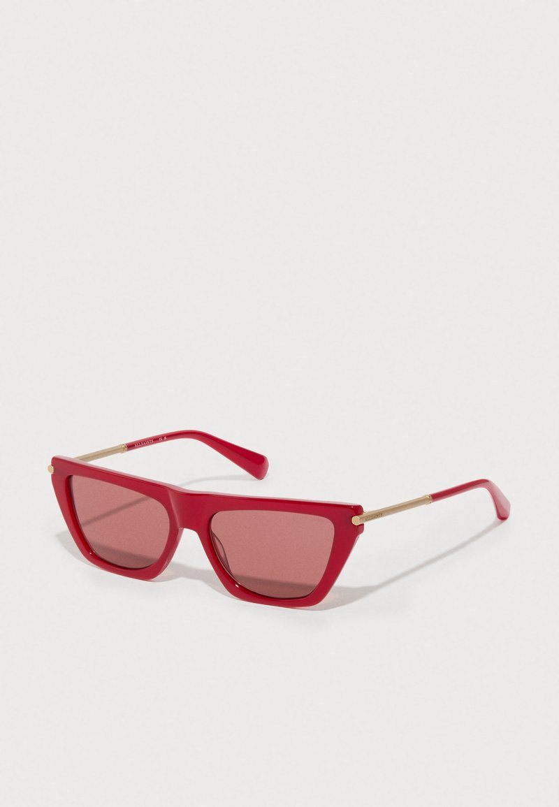 Óculos de sol retangulares vermelhos com hastes de metal dourado e lentes vermelhas tintadas em fundo branco.