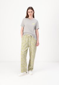 Szürke pamut póló sárga logóval, sárga mintás loungewear nadrággal párosítva, amely húzózsinórral ellátott derékrésszel rendelkezik, valamint fehér tornacipővel.