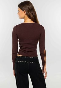 Top de manga larga de canalé en color burdeos con recortes en los puños. Combinado con pantalones negros holgados que tienen una cinturilla con tachuelas.