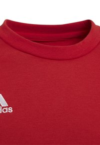 Tessuto a coste rosso con colletto alto, caratterizzato da un logo ricamato bianco. Il materiale appare morbido e aderente, con cuciture minime.