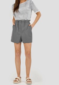 Szare bawełniane szorty z elastycznym pasem i bocznymi kieszeniami, stylizowane z luźną, jasnoszarym topem i beżowymi platformami.