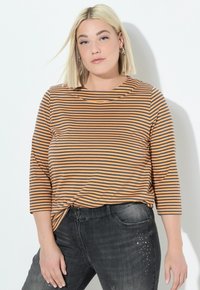 Gestreiftes Langarmshirt mit orangefarbenen und grauen horizontalen Streifen, runden Ausschnitt und lockerer Passform. Kombiniert mit dunklen Jeans aus Denim, die Verzierungen aufweisen.