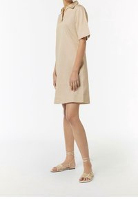 Vestido polo de algodón beige con mangas cortas y cuello, con un corte relajado. Llevado con sandalias planas desnudas de tiras.