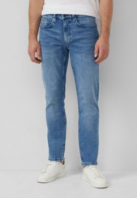Helle blaues Denim-Jeans mit Slim Fit, Fünf-Taschen-Design und dezenten Verwaschungen. Kombiniert mit weißen Sneakers vor einem neutralen Hintergrund.