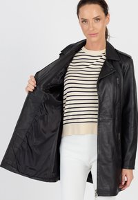 Schwarze Lederjacke mit Reverskragen, Reißverschlusstaschen und gerippten Bündchen, geöffnet, um ein glattes Innenfutter zu zeigen; getragen über einem gestreiften Oberteil.