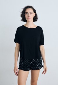 Fekete, rövid ujjú, cropped póló zsebbel, fekete pöttyös sorttal párosítva, amelynek fodros szegélye van.